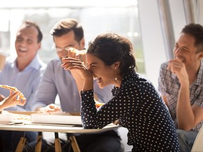 Indian woman laughing eating pizza with diverse coworkers in office