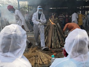 A family member (centre) wearing protective gear performs the last rites of a victim who died of COVID-19 at a crematorium in Ghazipur, India, Saturday, May 1, 2021.