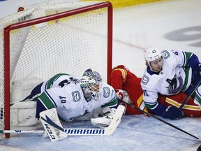 Vancouver Canucks goalie Braden Holtby, left, and Quinn Hughes, right, crash into the net with Calgary Flames' Elias Lindholm from scoring during third period NHL hockey action in Calgary, Wednesday, May 19, 2021.