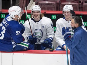 Vancouver Canucks' Adam Gaudette, second left, laughs while sitting on the bench with Bo Horvat, left, and Tyler Myers as head coach Travis Green, front right, stands on the ice.