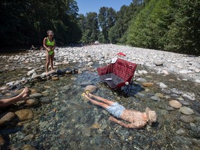 Albert Huynh cools off in the frigid Lynn Creek water as Leanne Opuyes, left, laughs in North Vancouver, B.C., on Monday, June 28, 2021. Environment Canada warns the torrid heat wave that has settled over much of Western Canada won't lift for days, although parts of British Columbia and Yukon could see some relief sooner.