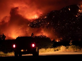 A motorist watches from a pullout on the Trans-Canada Highway as a wildfire burns on the side of a mountain in Lytton, Thursday, July 1, 2021.