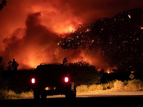 A motorist watches from a pullout on the Trans-Canada Highway as a wildfire burns on the side of a mountain in Lytton on Thursday, July 1, 2021.