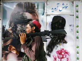 A Taliban fighter walks past a beauty saloon with images of women defaced using a spray paint in Shar-e-Naw in Kabul on August 18, 2021.