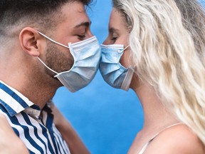 Young couple kissing while wearing face surgical mask during corona virus outbreak - Man and woman with facemask having romantic moments - People love relationship and coronavirus prevention concept