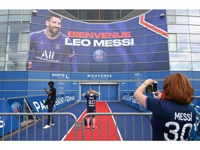 A woman takes a picture of her son on the red carpet in front of a large banner reading 'Welcome Leo Messi' on a wall of the Paris Saint-Germain's (PSG) Parc des Princes stadium in Paris on August 11, 2021. - Determined queues formed before dawn in front of the club boutique and roucous crowds gathered outside the stadium on August 11 as Lionel Messi was officially unveiled as a Paris Saint-Germain player.
