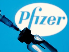 A vial and syringe are seen in front of a displayed Pfizer logo in this illustration taken January 11, 2021.