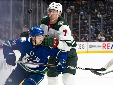 VANCOUVER, BC - OCTOBER 26: Quinn Hughes #43 of the Vancouver Canucks and Nico Sturm #7 of the Minnesota Wild battle for the loose puck along the boards during the first period of NHL action on October, 26, 2021 at Rogers Arena in Vancouver, British Columbia, Canada.