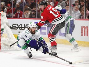 Conor Garland of the Vancouver Canucks knocks the puck away from Jonathan Toews of the Chicago Blackhawks at United Center on October 21, 2021 in Chicago, Illinois.