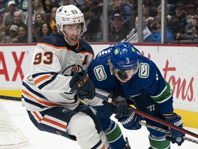 Edmonton Oilers' Ryan Nugent-Hopkins (left) and Vancouver Canucks' Jack Rathbone battle for the puck during first period NHL hockey action in Vancouver on Saturday, Oct. 30, 2021.