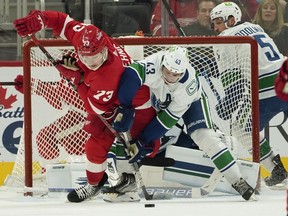 Detroit Red Wings left wing Adam Erne (73) and Vancouver Canucks defenseman Quinn Hughes (43) battle for the puck in the second period of an NHL hockey game Saturday, Oct. 16, 2021, in Detroit.