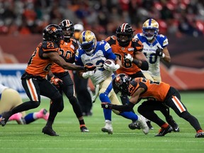 Winnipeg Blue Bombers' Andrew Harris, centre, is tackled by B.C. Lions' Anthony Thompson (23) and Jalon Edwards-Cooper (29) during the first half of a CFL football game in Vancouver, on Friday, October 1, 2021.