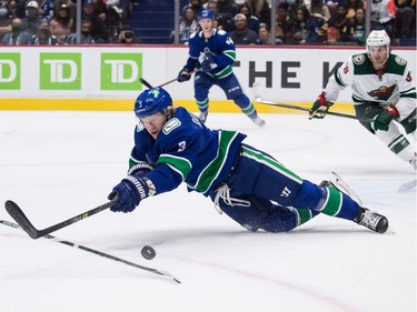 Vancouver Canucks' Jack Rathbone stumbles as he reaches for the puck during the first period of an NHL hockey game against the Minnesota Wild in Vancouver, on Tuesday, October 26, 2021.