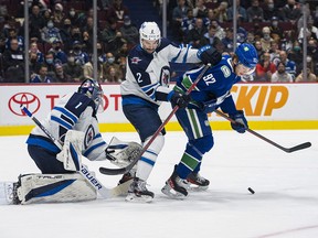 Winnipeg Jets goalie Eric Comrie looks away as defenceman Dylan DeMelo checks Vancouver Canucks forward Vasily Podkolzin in the first period at Rogers Arena.