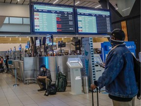 A passenger holds his mobile phone while looking at an electronic flight notice board displaying cancelled flights at OR Tambo International Airport in Johannesburg on November 27, 2021.
