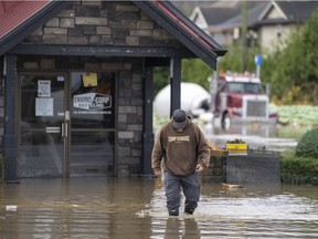 A man walks through the rising flood waters crossing into Canada from the United States in Huntington Village in Abbotsford, B.C., Monday, November 28, 2021.