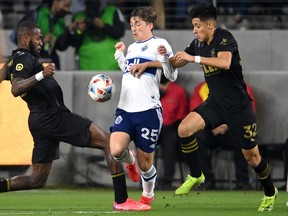 Los Angeles FC defender Sebastien Ibeagha (25), Vancouver Whitecaps midfielder Ryan Gauld (25), and Los Angeles FC defender Marco Farfan (32) go for the ball in the first half at Banc of California Stadium.