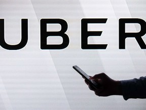 A man checks his smartphone while standing against an illuminated screen bearing the Uber logo in London on June 26, 2018.