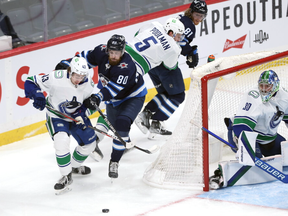 Winnipeg Jets centre Pierre-Luc Dubois (second from left) lays the lumber on Vancouver Canucks defenceman Quinn Hughes (left) in Winnipeg on Jan. 27.