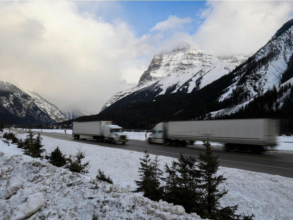 Semi-trailer trucks drive past snow-covered mountains along the Trans-Canada Highway 1 near Field, B.C