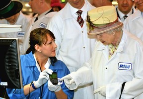 Queen Elizabeth II, wearing a white protective coat (R), is shown a new product, at the final testing before packaging test area during her tour of the RIM (Research In Motion) factory that produces the Blackberry mobile communications handset, on July 5, 2010 in Waterloo, Canada.