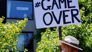 A pro-refugee protester holds a 'game over' sign outside the Park Hotel, where Serbian tennis player Novak Djokovic is believed to be held while he stays in Melbourne, Australia, on Jan. 9, 2022.