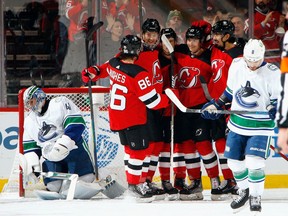 For Canucks goalie Jaroslav Halak, left, who was chased from the game, and winger Conor Garland, right, this was a sorry scene — a New Jersey Devils goal celebration — repeated too often on Monday in Newark, N.J.