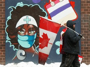 Decked out with flags, two protesters in Ottawa walk past a painting depicting a health-care professional wearing a mask.