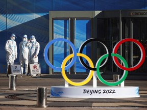 Workers in full protective gear stand next to the Olympic rings inside the closed loop area near the National Stadium, where the opening and closing ceremonies of Beijing 2022 Winter Olympics will be held.