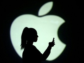 Silhouette of mobile user is seen next to a screen projection of Apple logo in this picture illustration taken March 28, 2018.