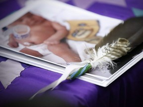 A proposed class action has been filed against Manitoba government by a woman who had her newborn removed by police and social workers in a video broadcast live on social media. An eagle feather and a baby hospital ID bracelet sit on a photo of a newborn baby during a news conference in Winnipeg on Friday, Jan. 11, 2019, in support of the mother whose newborn baby was seized from hospital by Manitoba's Child and Family Services. John Woods/Canadian Press