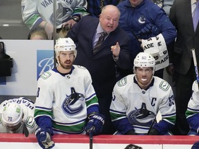 Vancouver Canucks coach Bruce Boudreau, back, argues for a call with an official, during the third period of the team's NHL hockey game against the Colorado Avalanche on Wednesday, March 23, 2022, in Denver.