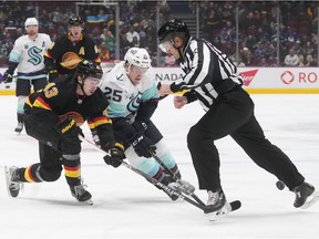 Vancouver Canucks' Quinn Hughes (43) and Seattle Kraken's Karson Kuhlman (25) vie for the puck as linesman Bryan Pancich tries to get out of the way during the first period of an NHL hockey game in Vancouver, on Tuesday, April 26, 2022.