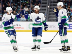 Conor Garland (middle) of the Vancouver Canucks celebrates his goal with Quinn Hughes (left) and Luke Schenn during the third period against the Seattle Kraken at Climate Pledge Arena on January 1, 2022 in Seattle, Washington.