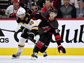 Matt Grzelcyk of the Boston Bruins (left) and Jesperi Kotkaniemi of the Carolina Hurricanes battle during a May 4, 2022 Stanley Cup playoff game in Raleigh, N.C.