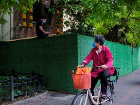 A woman passes a resident sitting on a barrier as she rides a bicycle at a closed residential area during lockdown, amid the COVID-19 outbreak, in Shanghai, May 30, 2022.