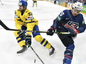 Zviedrijas aizsargs Olivers Ekmans-Larsons (pa kreisi) sacenšas par ripu ar amerikāņu uzbrucēju Kārsonu Kolmanu IIHF pasaules hokeja čempionāta B grupas pirmās kārtas spēlē starp ASV un Zviedriju Tamperē, Somijā, 2022. gada 21. maijā. / Lehtikuva/AFP)/