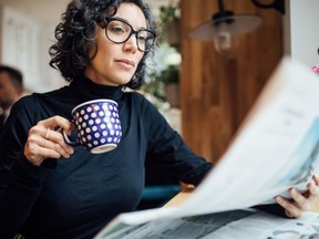 A woman reading a newspaper and having coffee.