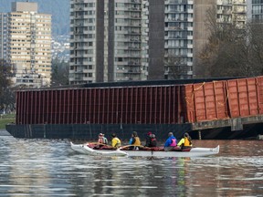 A canoe moves past a large barge that continues to sit on the rocks on Sunset Beach in Vancouver, BC, November, 21, 2021.