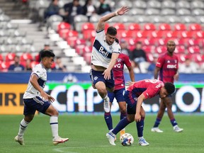 Vancouver Whitecaps' Lucas Cavallini, centre, leaps to avoid FC Dallas' Brandon Servania, right, as Vancouver's Michael Baldisimo, left, watches during the first half of an MLS soccer game in Vancouver, on Wednesday, May 18, 2022.