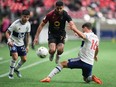 Valour FC's Federico Pena (77) jumps to avoid the tackle by Vancouver Whitecaps' Sebastian Berhalter (16) as Ryan Raposo (27) watches during the first half of a preliminary round Canadian Championship soccer match, in Vancouver, on Wednesday, May 11, 2022.