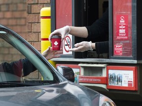 A Tim Hortons employee hands out coffee from a drive-thru window to a customer in Mississauga, Ont., on March 17, 2020.