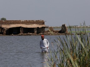 A flood victim man wades through flood water with a damaged house in the background, following rains and floods during the monsoon season in Gari Yasin, Shikarpur, Pakistan Aug. 31, 2022.