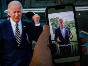 In this photo illustration taken on July 21, 2022 in Washington, DC, a video tweet from US President Joe Biden is seen on a cell phone, juxtaposed on a computer screen in the background, with a breaking news alert that the President has tested positive for the coronavirus.