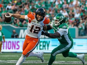 B.C. Lions quarterback Nathan Rourke evades a tackle from Saskatchewan Roughriders defensive lineman Charleston Hughes during their July 29, 2022 Canadian Football League game in Regina.