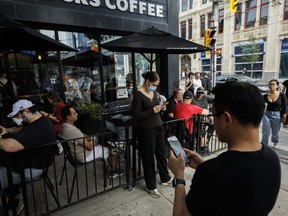 People use electronics outside a coffee shop in Toronto amid a nationwide Rogers outage, affecting many of the telecommunication company's services, Friday, July 8, 2022.