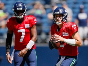 Seattle Seahawks quarterback Drew Lock, center, drops back to pass as Geno Smith, left, watches before a mock NFL football game, Saturday, Aug. 6, 2022, in Seattle.