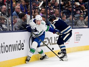 Quinn Hughe of the Vancouver Canucks and Sean Kuraly of the Columbus Blue Jackets compete for the puck along the boards during the second period at Nationwide Arena on October 18, 2022 in Columbus, Ohio.