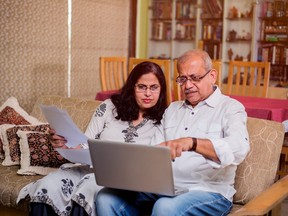 Senior Indian/asian couple accounting, doing home finance and checking bills with laptop, calculator and money while sitting at home garden