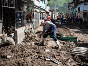 A man removes mud from the front of his house with a pickaxe in Las Tejerias, Venezuela, Tuesday, Oct. 11, 2022.